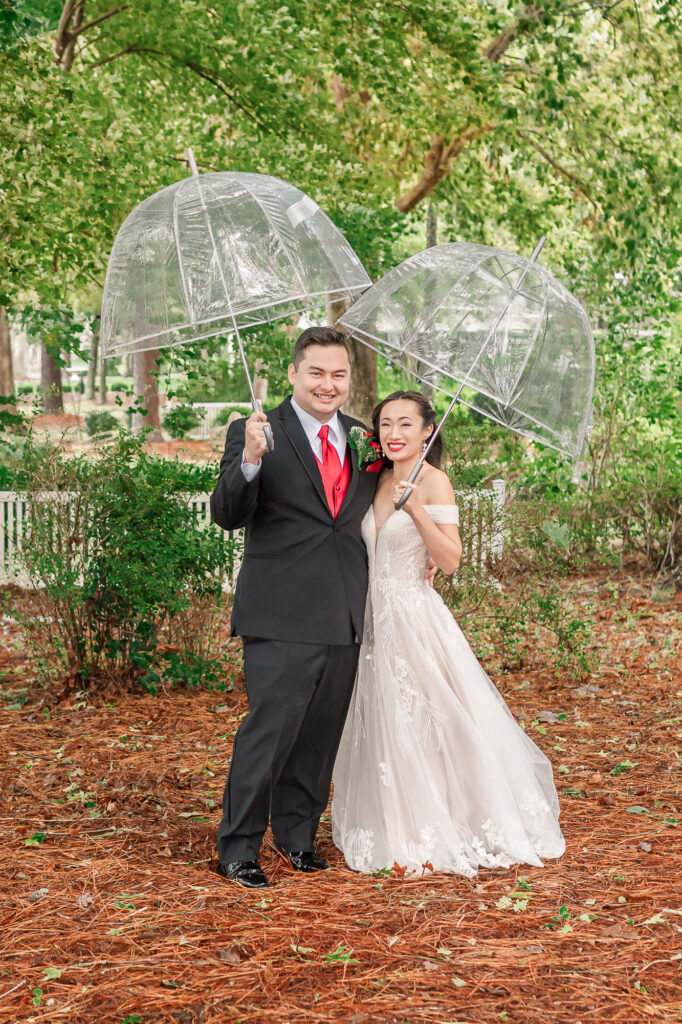 A happy couple holding umbrellas in the rain on their Lake Gaston Wedding Day