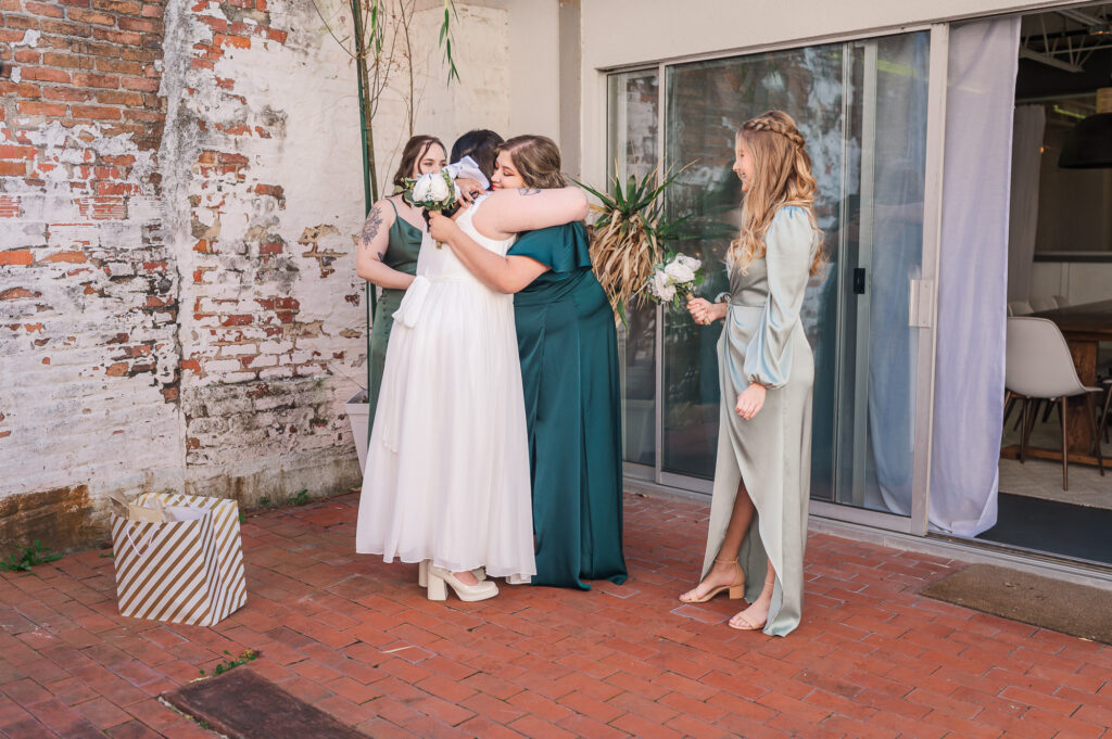 A bride and her bridesmaids hugging and celebrating her wedding day The Atrium Wedding Venue by JoLynn Photography