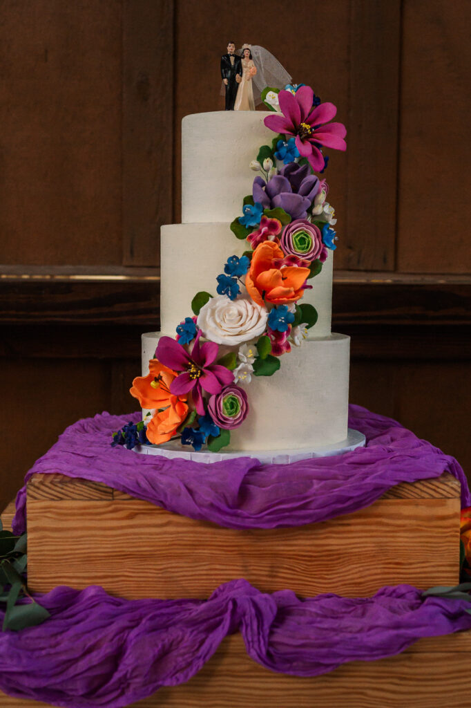 A warm wedding cake of orange and purple flowers at the River Landing wedding venue by JoLynn Photography