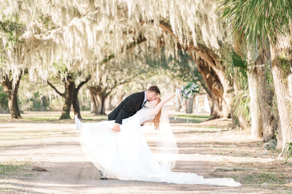 A newly wed couple kissing under Spanish moss trees at Savannah Destination Wedding by JoLynn Photography