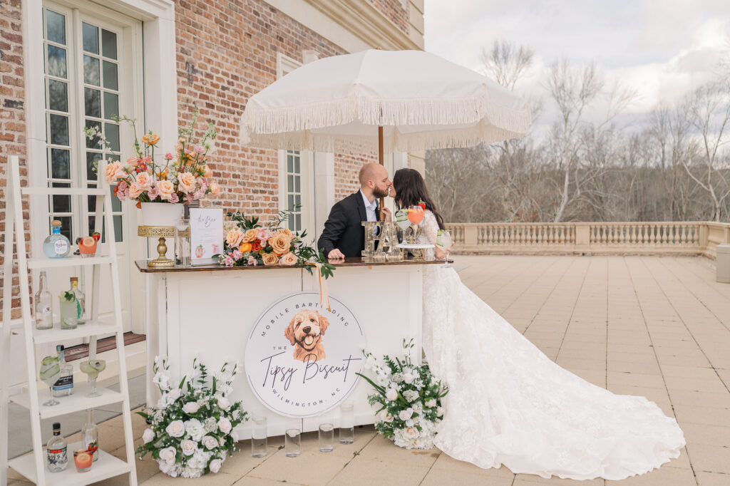 A husband and wife kissing in front of a bar cart at The Oxbow Estate by JoLynn Photography