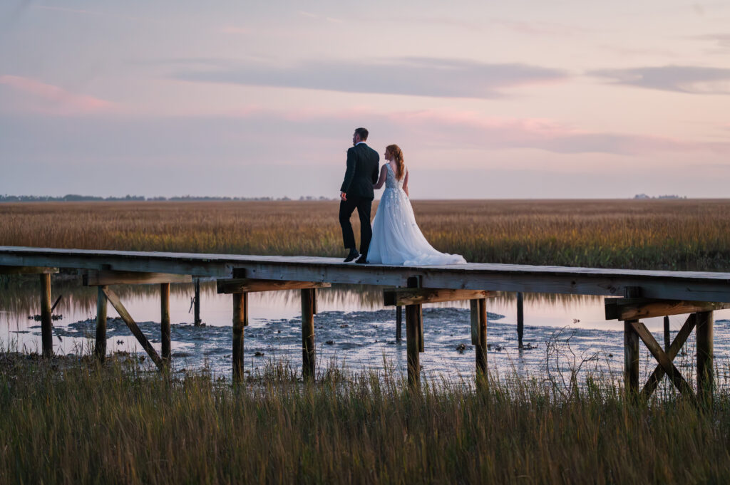 A married couple walking over freshwater ponds at sunset at a Savannah Destination Wedding by JoLynn Photography