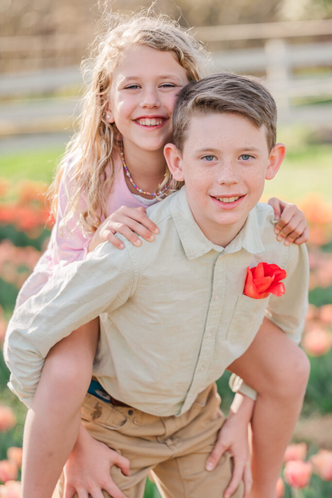 A happy brother and sister playing piggyback during their spring family portraits by JoLynn Photography, a Greensboro family photographer