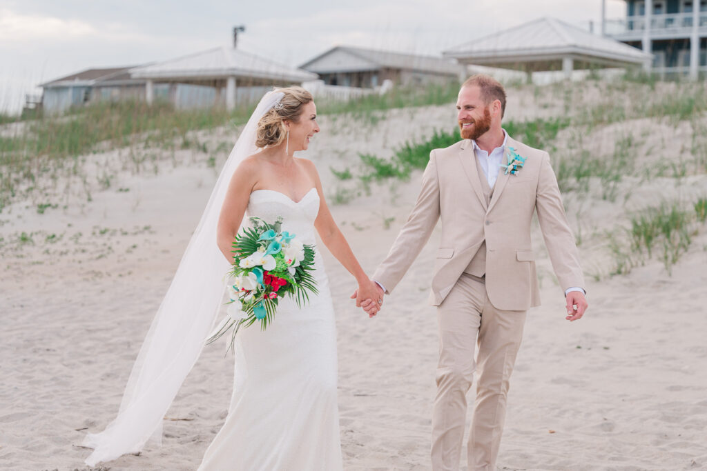 A happy newly married couple walking down the beach enjoying their Atlantic beach wedding by JoLynn Photography