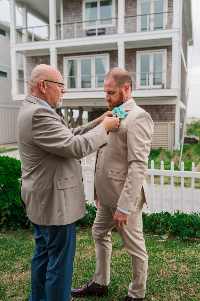 A dad helping button his son's wedding jacket at this Atlantic beach wedding 