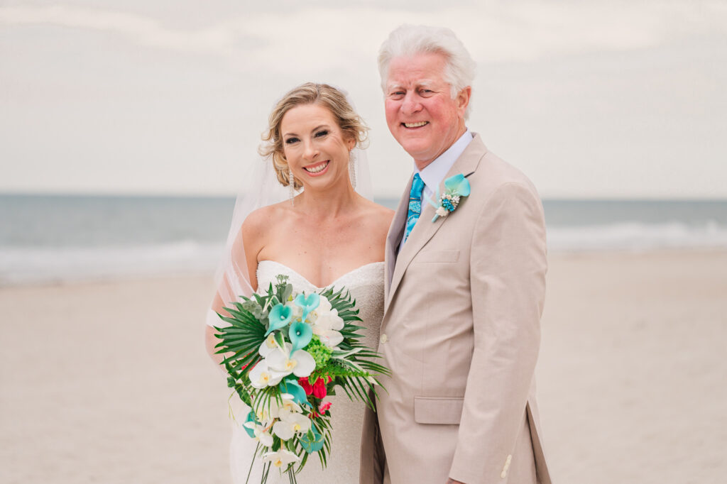 Smiling blonde bride and her dad on the beach on her wedding day by JoLynn Photography