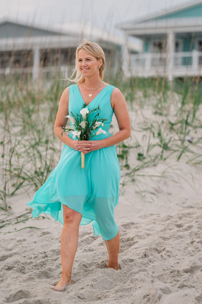 A bridesmaid in a teal bridesmaid dress walking down the beachside aisle in Atlantic Beach