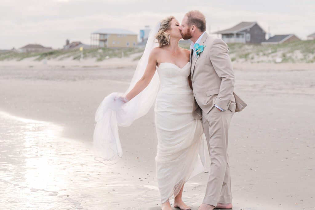 A newly married bride and groom kissing during their Atlantic Beach wedding at sunset by JoLynn Photography