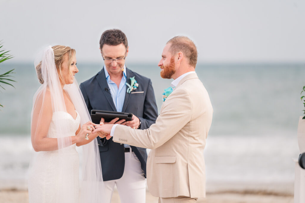 A bride placing a wedding band on her new husband during their Atlantic beach wedding by JoLynn Photography