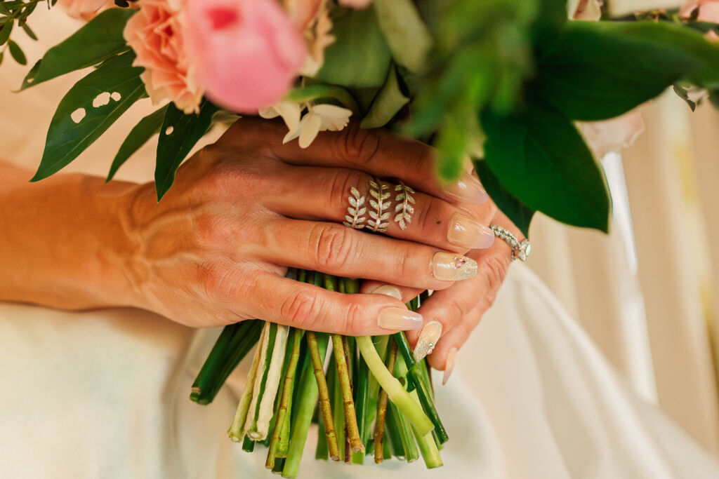 A bride holding a bridal bouquet with diamond rings on her fingers by JoLynn Photography