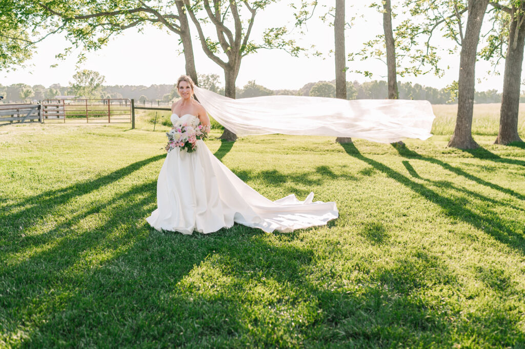 A smiling bride at sunset as her wedding veil is flying at Highrock Farms by JoLynn Photography