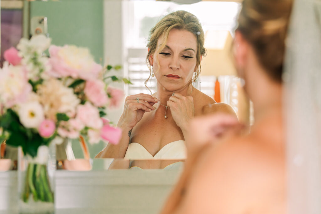 A happy bride putting her wedding necklace on her bridal suite mirror