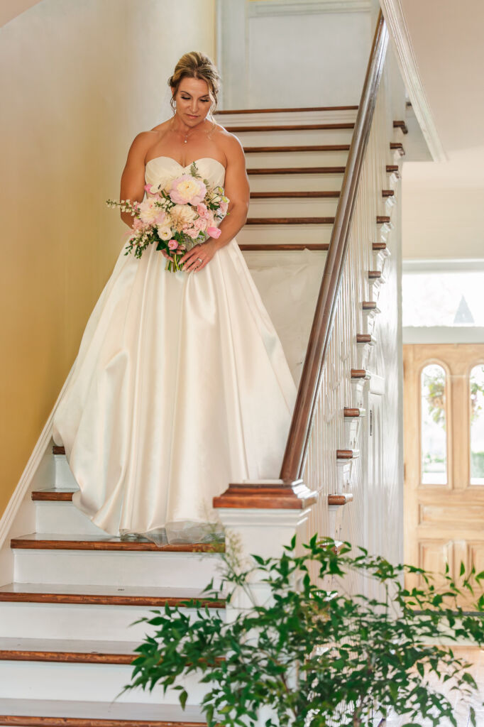 A loving bride standing in the stairway with her bridal bouquet at Highrock Farms by JoLynn Photography 