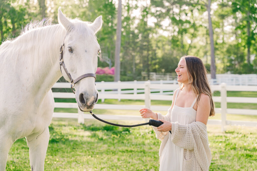 A smiling bride to be playing with a white horse during her engagement session in Wilmington by JoLynn Photography