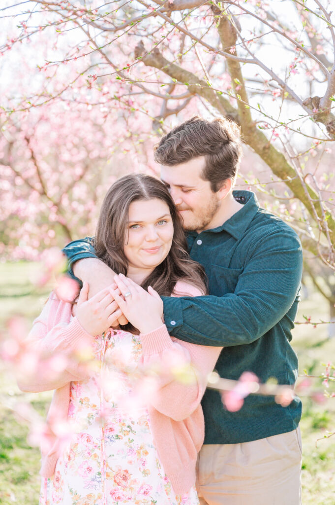 A bubbly and happy engaged couple enjoying their Greensboro engagement under cherry blossom trees by JoLynn Photography