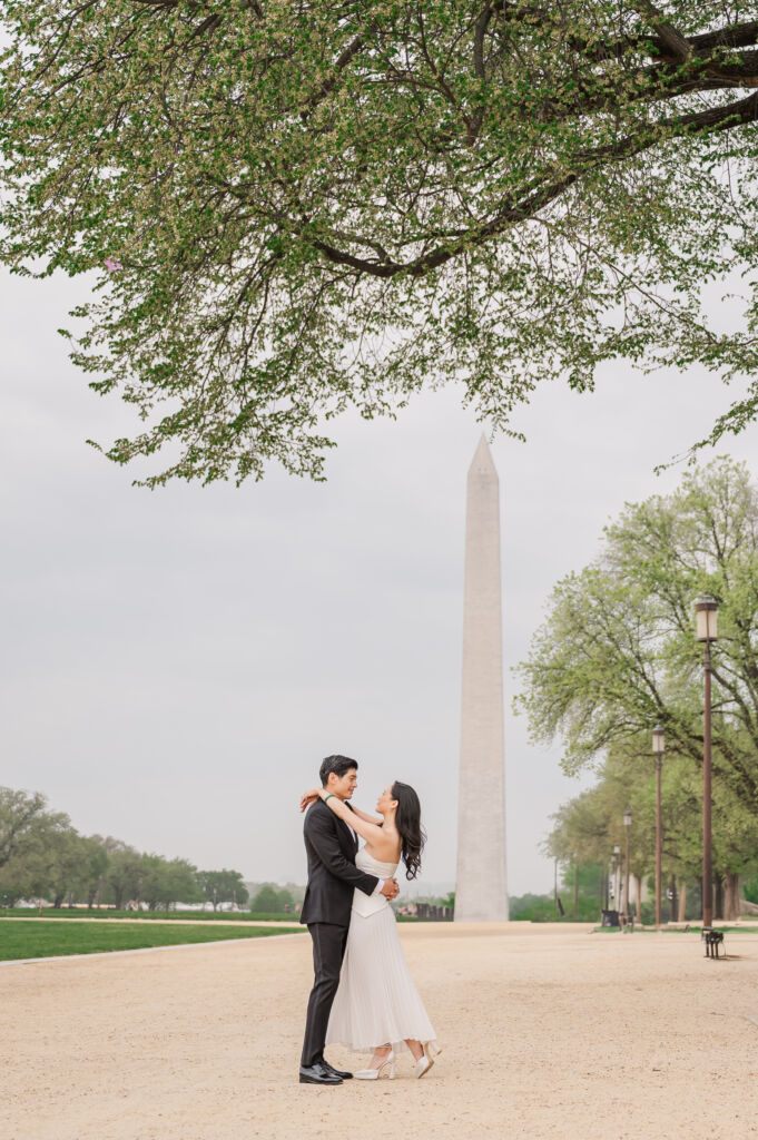 A loving happy Asian couple celebrating their spring engagement next to iconic DC monuments by Washington DC wedding photographer, JoLynn Photography