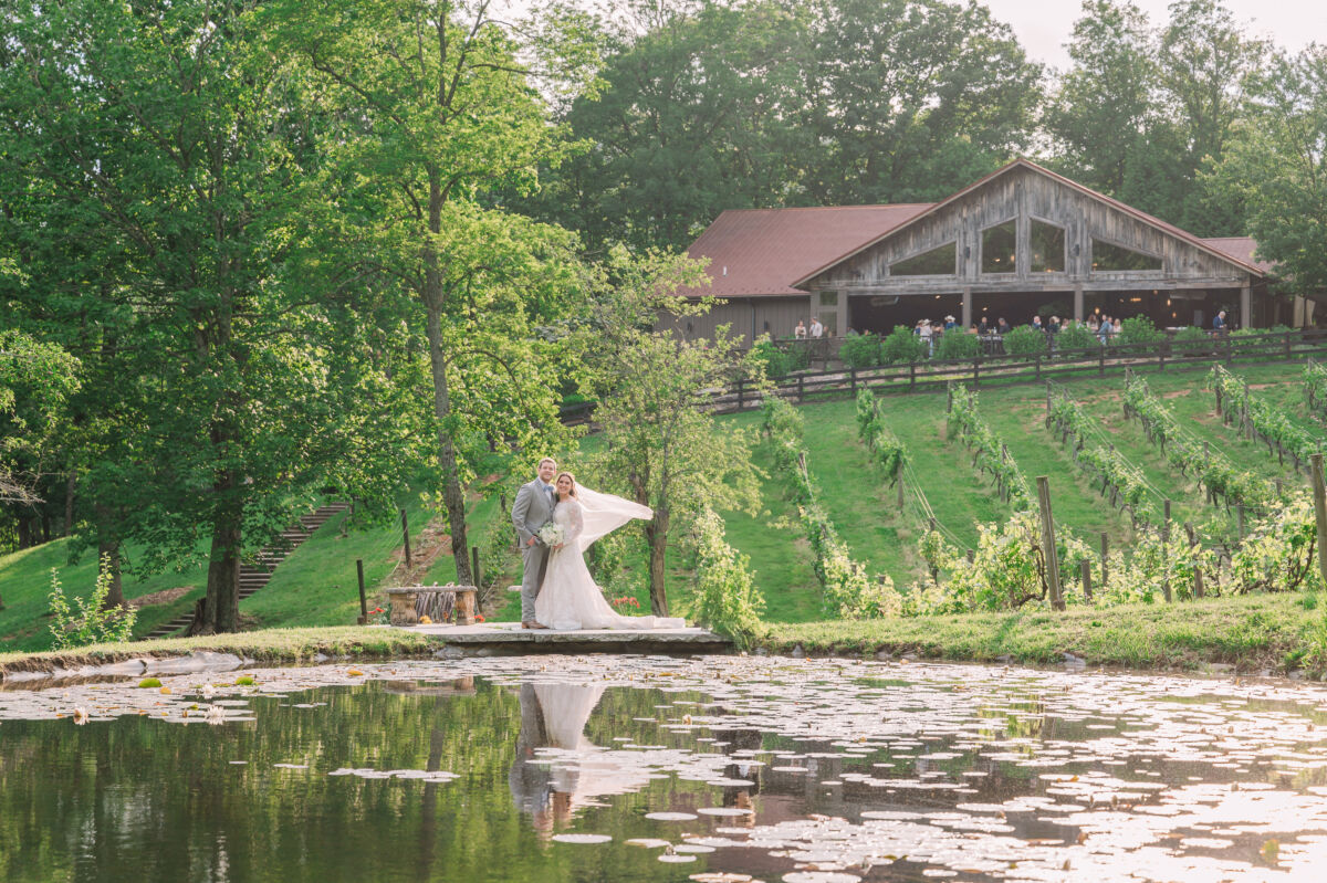 A happy newly married couple overlooking water as the sun is setting on a summer wedding day at the Vineyard at High Holly by JoLynn Photography