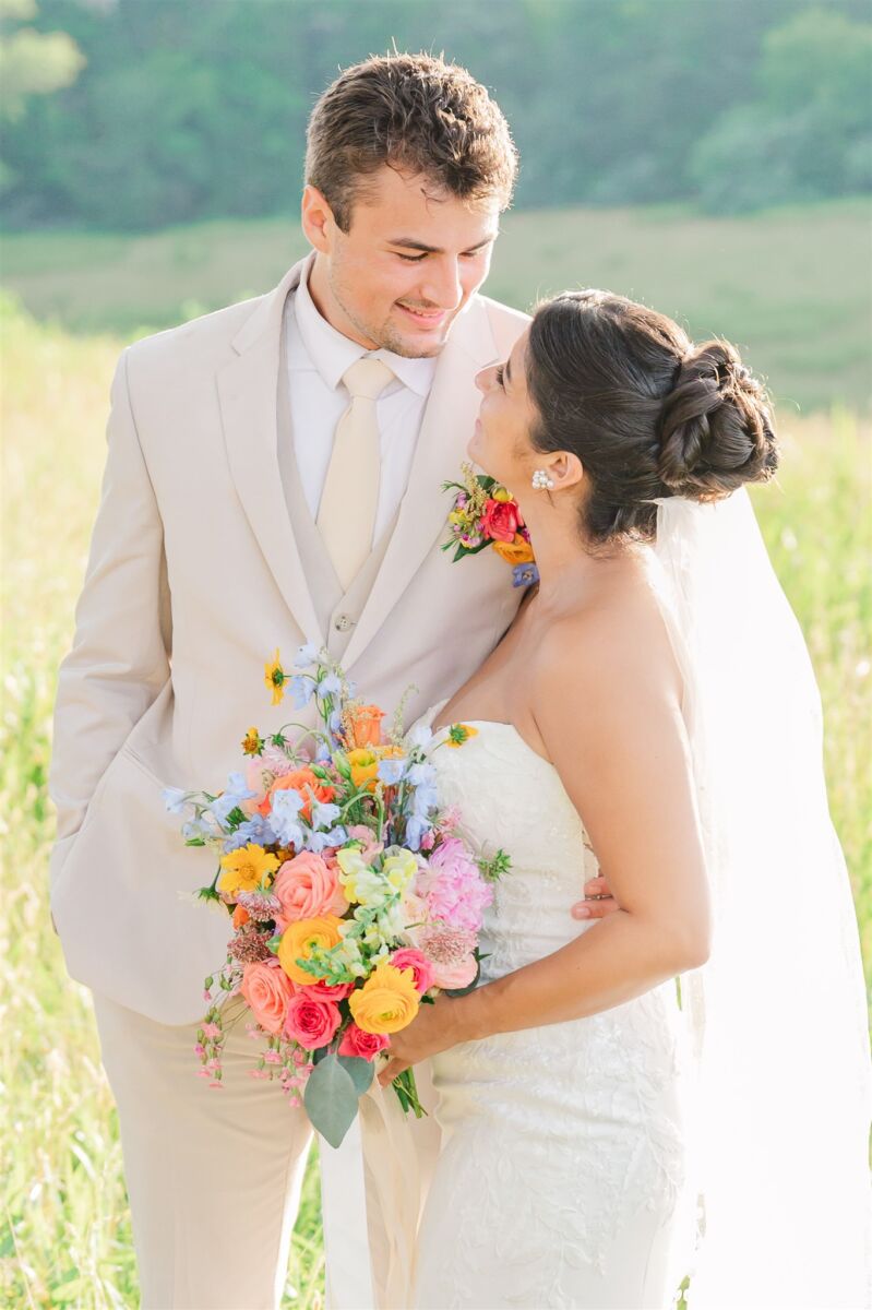 Newlyweds smile at each other with arms around each other in a meadow during their Duplin Winery wedding