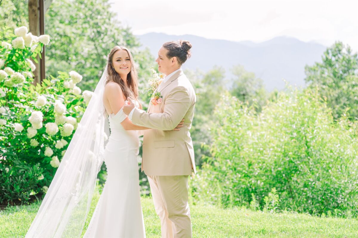 Newlyweds stand on a hillside with some flowers cuddling during their Duplin Winery wedding