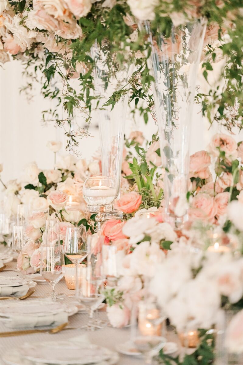 Details of a wedding reception table covered in pink roses with clear glasses and gold silverware at one of the Garner wedding venues