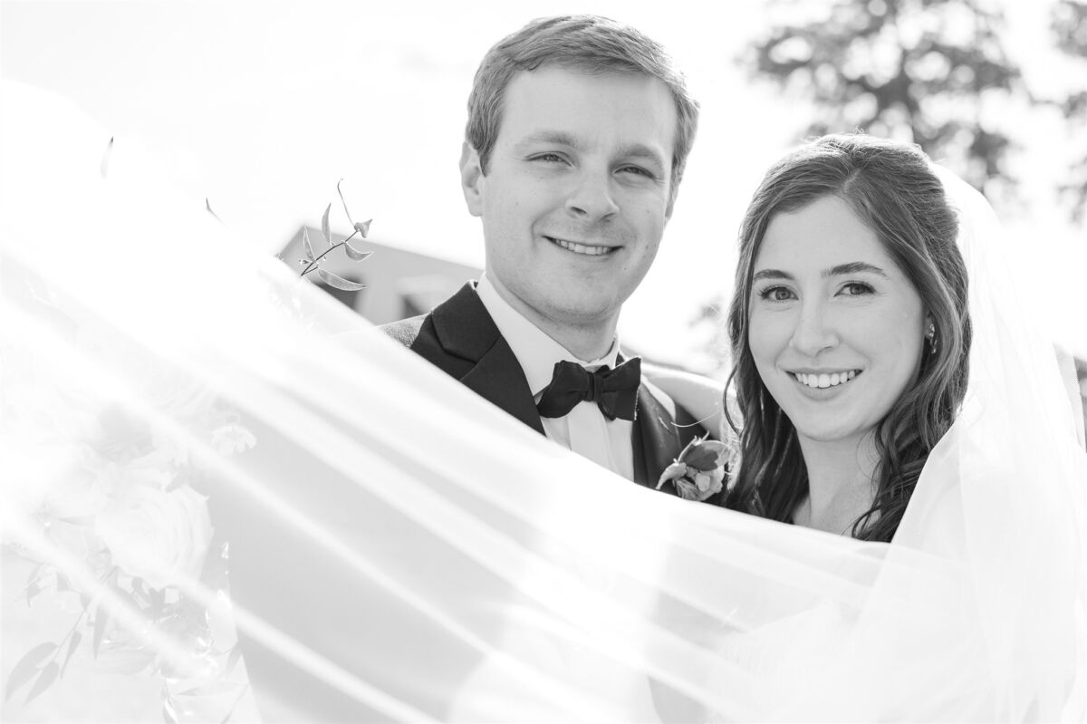 Happy newlyweds smile together while standing in a garden as the veil flies around them