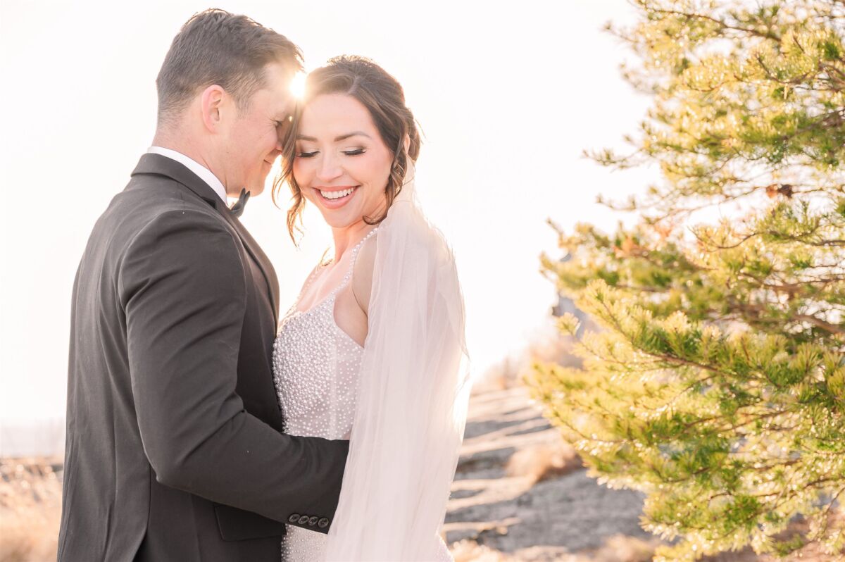 A bride smiles down her shoulder while snuggling her groom at sunset on the side of a mountain at one of the North Carolina mountain wedding venues