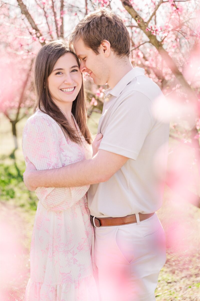 A happy engaged couple snuggles among the cherry blossoms with big smiles after finding Greensboro wedding planners