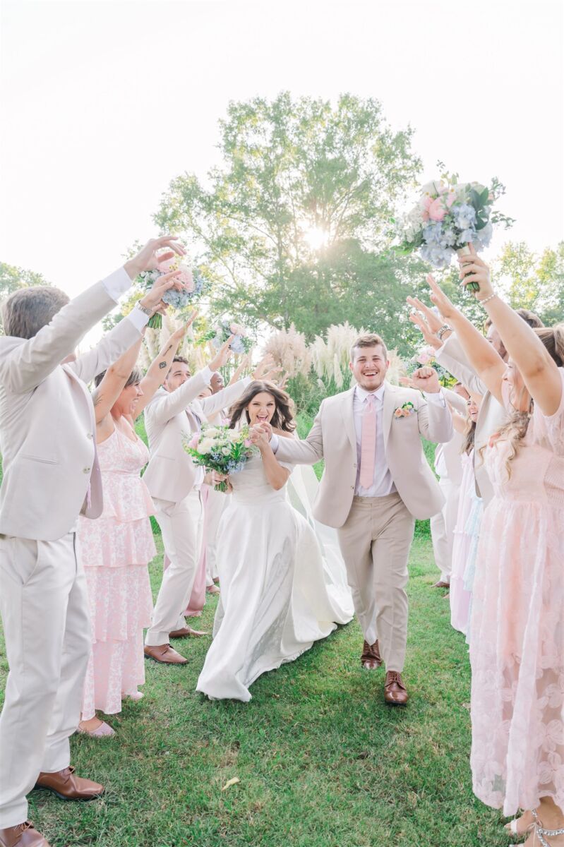 Newlyweds cheer wile running under the arms of their wedding party in a meadow