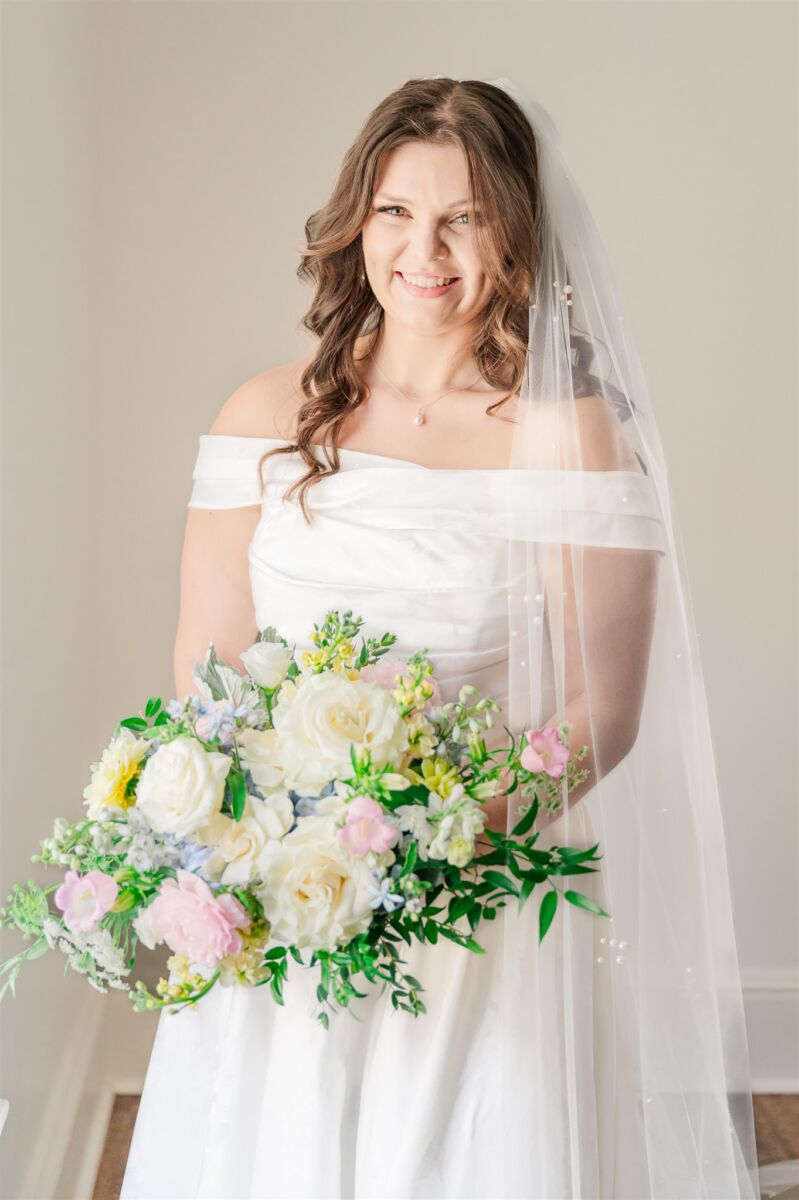 A happy bride smiles in her gown in the getting ready suite holding her white and pink bouquet at her Rose Hill Estate Wedding