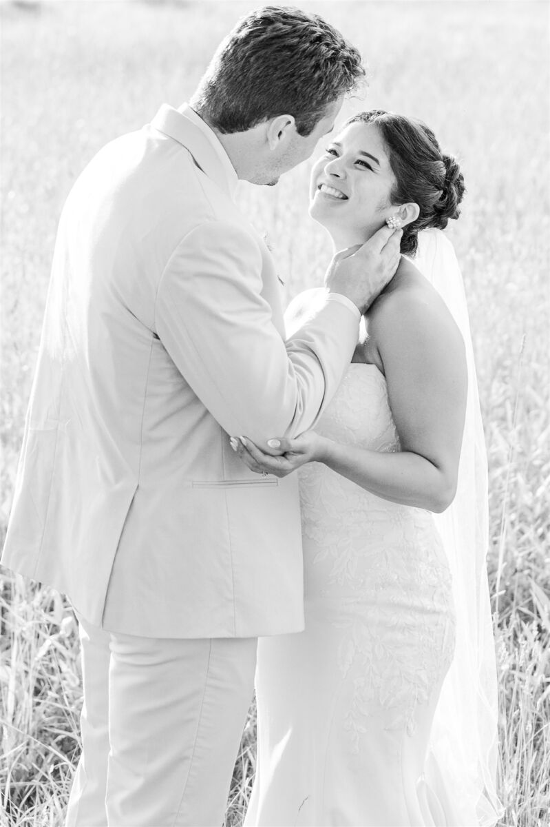 Newlyweds laugh and share a quiet moment standing in tall grass in black and white at The Club At 12 Oaks wedding venue