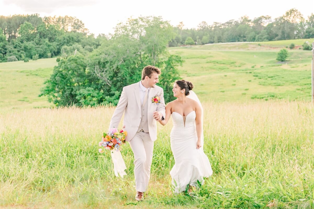 Happy newlyweds holding hands walking up a hill at sunset holding a colorful bouquet