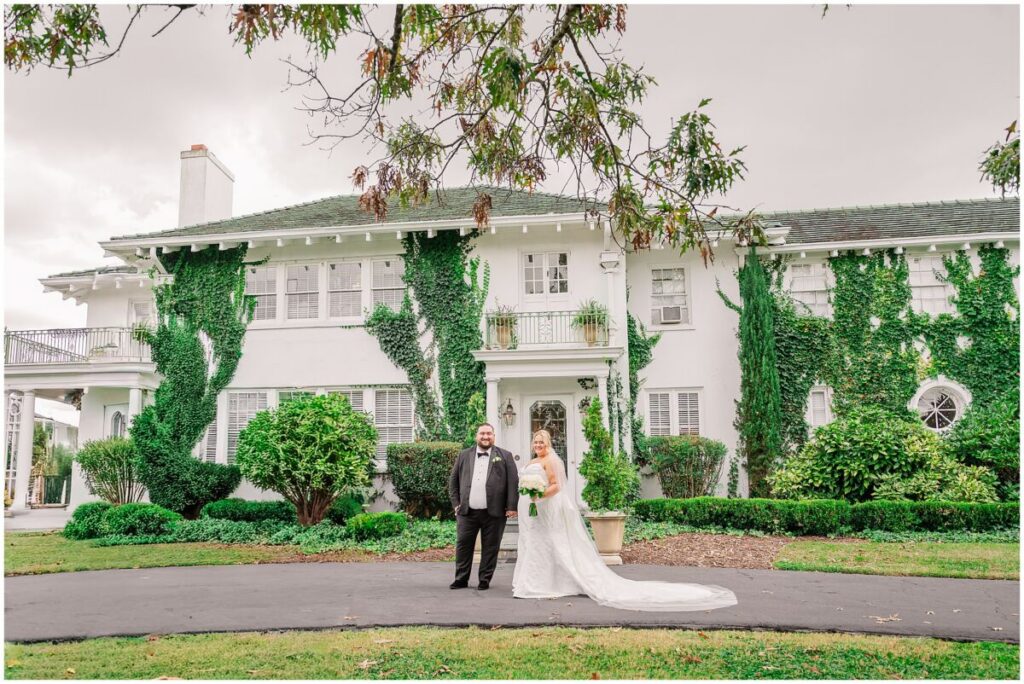 A glowing blonde bride and her husband in an all black tux on a stunning summer wedding day at The Finch House enjoying their wedding portraits by JoLynn Photography