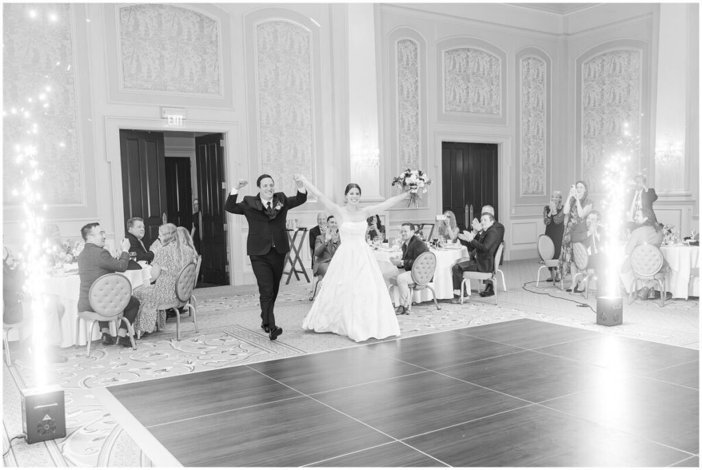 A happy couple entering their wedding reception surrounded by family and friends while sparklers go off during their Cary wedding by JoLynn Photography