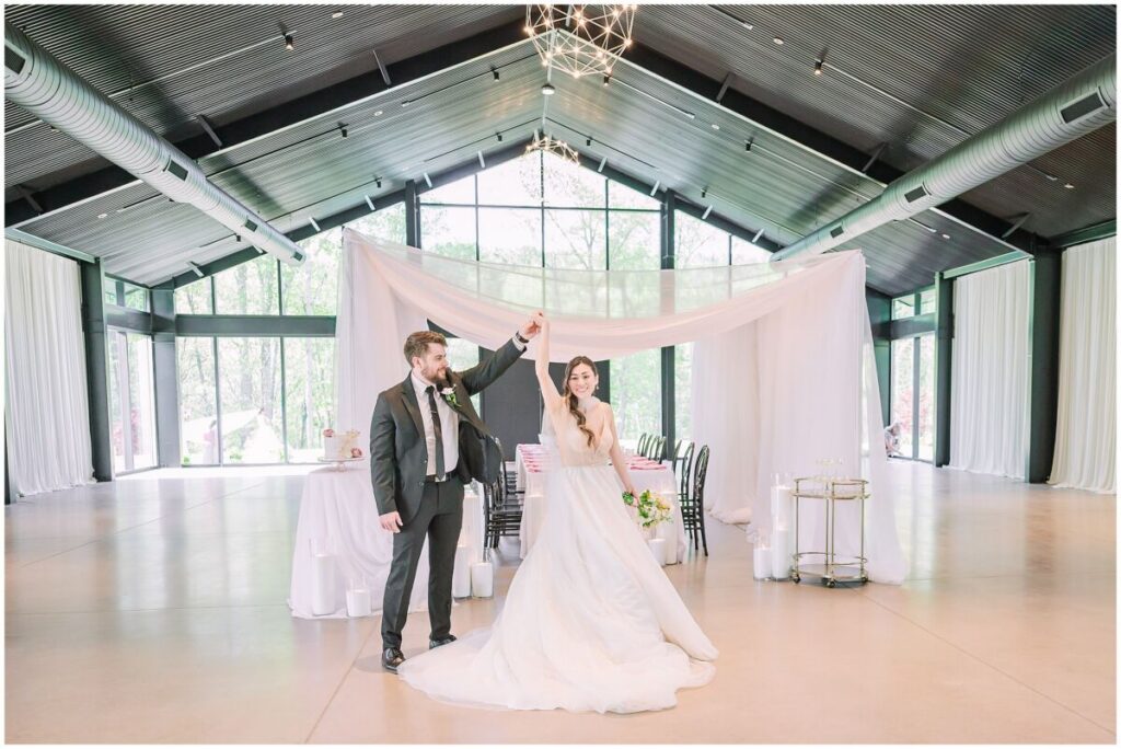A happy brunette couple sharing a dance during their spring wedding surrounded by pink flowers and warm lighting at The Skyroom by JoLynn Photography