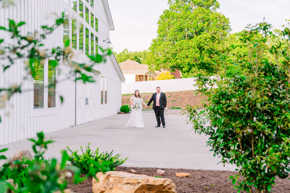 A happy couple holding hands during their wedding day at The Barn at Blue Sky Farm at sunset surrounded by soft greenery by JoLynn Photography