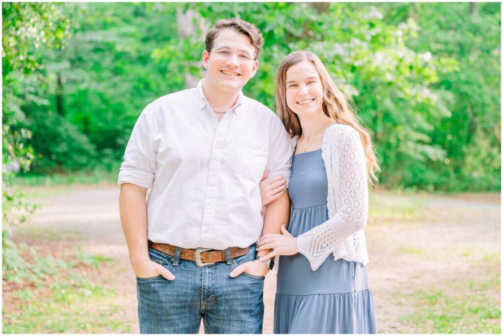 A happy couple wearing  a timeless balance of blue and white during their summer Yates Mill engagement by JoLynn Photography in the woods at sunset