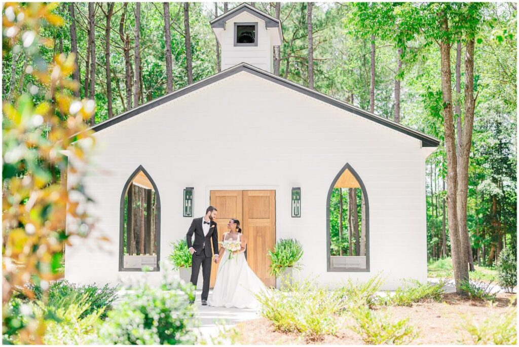 A loving couple holding hands and walking outside of an open air chapel at Stone Manor during the summer sunset by JoLynn Photography