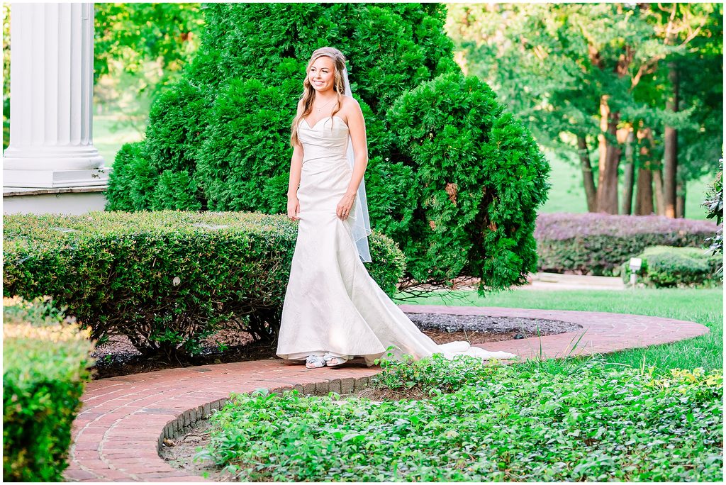 A Rose Hill Estate bridal portrait of a glowing bride walking through an evergreen garden on a stunning brick pathway by JoLynn PHotography